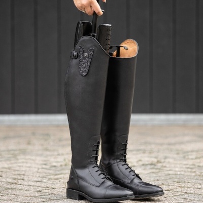 Botas altas pretas em couro sintético com atacadores e detalhes decorativos sobre chão pavimentado.