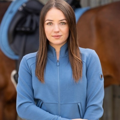 Mulher de casaco azul com cavalo e sela azul ao fundo