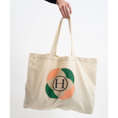Saco de tecido bege com estampa circular verde e salmão com a letra H no centro