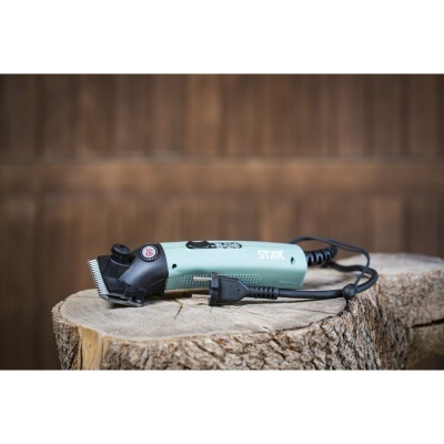 Máquina de cortar cabelo elétrica verde claro com lâmina metálica sobre tronco de árvore