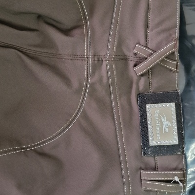 Calças castanhas com costuras brancas e etiquetas da marca Equi-Thème