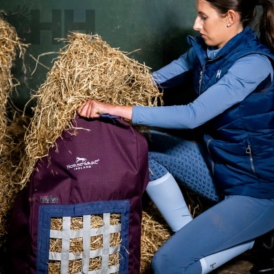 Mulher a encher saco de feno bordô HORSEWARE IRELAND em estábulo