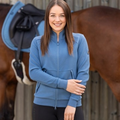 Mulher com casaco azul junto a cavalo castanho com sela