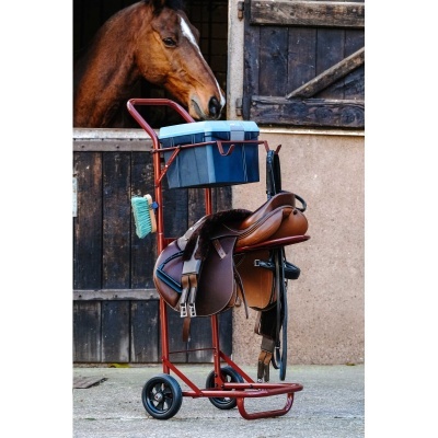 Carrinho com sela de couro e caixa plástica em frente a porta de estábulo com cavalo