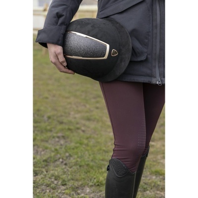 Capacete de equitação preto com detalhe dourado segurado por pessoa com roupa de equitação
