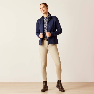 Mulher com casaco azul escuro, camisola com padrão azul claro, calças bege e botas castanhas em fundo branco.