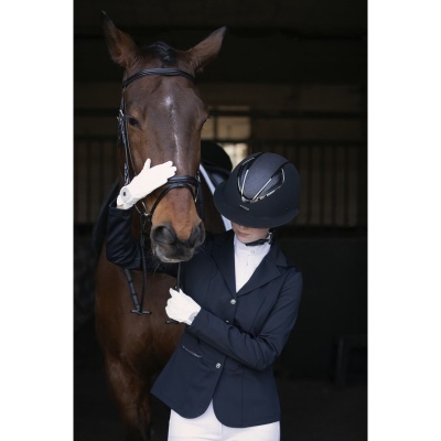 Cavalo castanho com cabeçada preta e cavaleira em roupa de competição num estábulo.