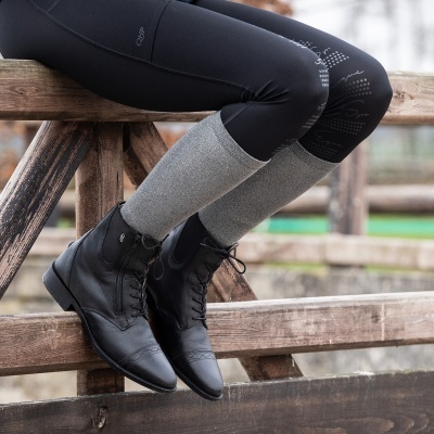 Botas pretas de couro com atacadores e polainas cinza claro sentada num corrimão de madeira