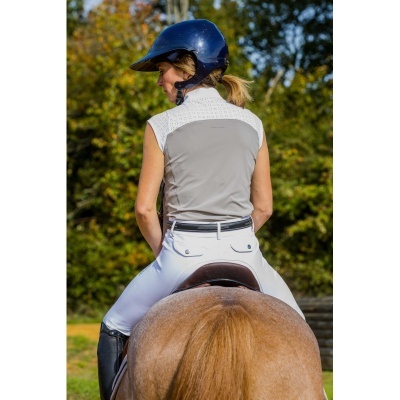 Mulher montando cavalo com capacete azul e roupa de equitação branca e bege