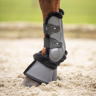 Proteções cinzentas para pernas de cavalo com forro preto em pelúcia num campo arenoso