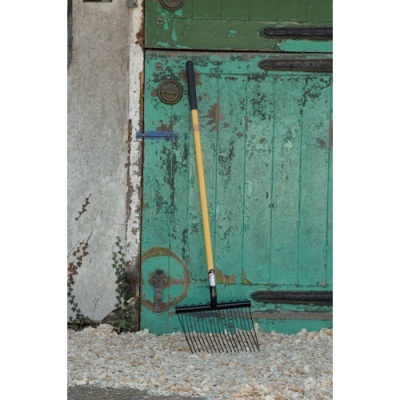 Ancinho de jardim com cabo amarelo e ponteira preta junto a porta verde antiga com cascalho no chão