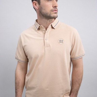 Homem a vestir polo bege de manga curta com botão e letras TH no peito