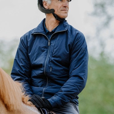 Homem de jaqueta azul e capacete cinza sentado num cavalo castanho claro.
