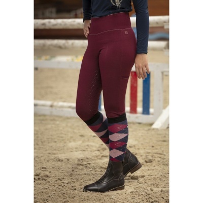 Leggings bordeaux com padrão geométrico e botas pretas numa pista de areia para equitação