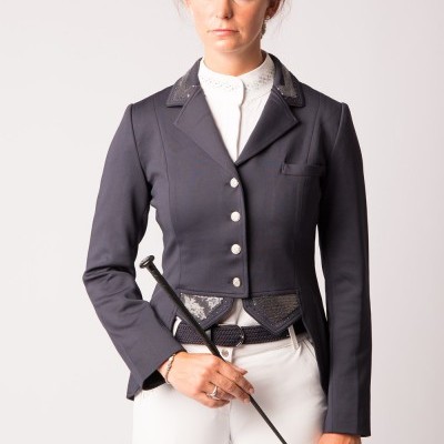 Mulher com casaco equestre azul escuro, camisa branca e calças brancas, segurando vara preta.