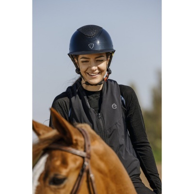 Mulher com capacete azul e colete preto a montar cavalo castanho ao ar livre