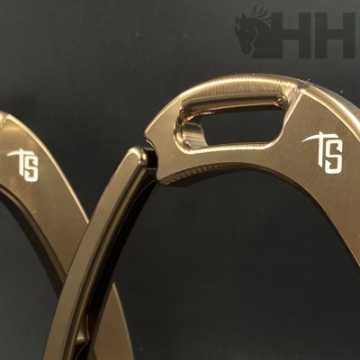 Detalhe de ferraduras metálicas douradas com logo TS em fundo preto.