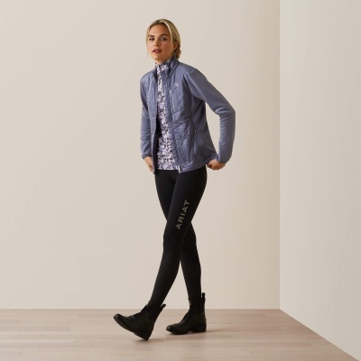 Mulher com casaco azul, blusa branca floral, leggings pretas ARIAT e botas pretas