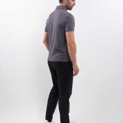 Homem de pé com polo cinzento escuro, calças pretas e sapatilhas brancas