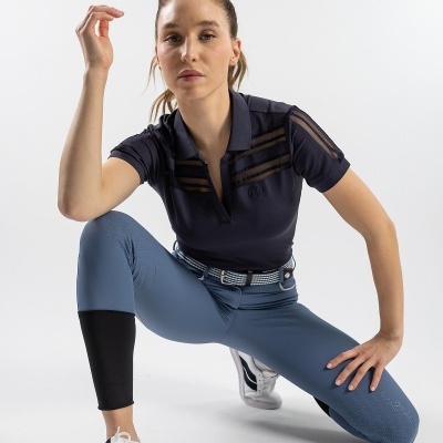 Mulher com camisa polo preta, calças justas azul claro e sapatilhas brancas em fundo branco