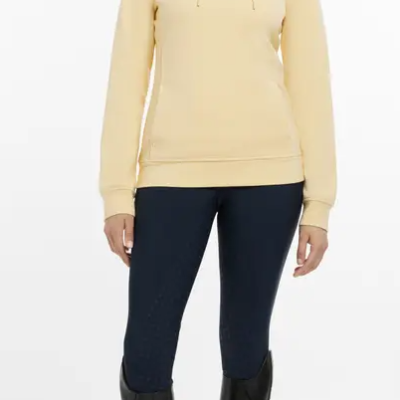 Mulher com sweatshirt amarela clara de capuz, jeans escuros e botas pretas altas.