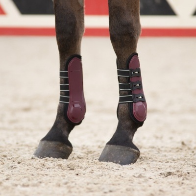 Botas de proteção bordô e pretas para patas de cavalo em piso de areia