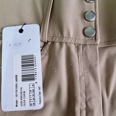 Calças bege com botões prateados e etiqueta com código de barras e texto