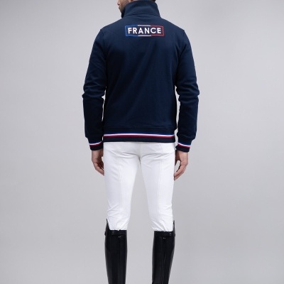 Casaco azul escuro com a palavra FRANCE nas costas, usado por homem com calças brancas e botas pretas.