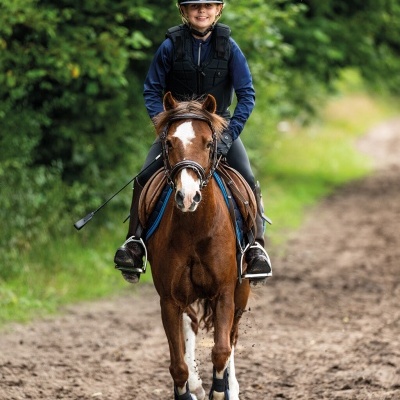 Pessoa montada a cavalo num caminho de terra com vegetação verde ao fundo