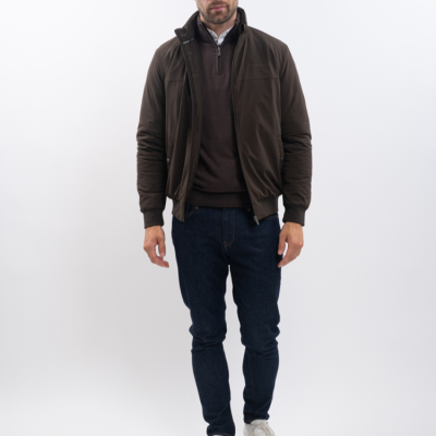 Homem com casaco castanho, camisola castanha, camisa branca, jeans azul e ténis brancos em fundo branco.