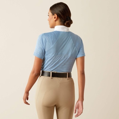 Mulher vista de costas com camisa azul clara e calças bege num fundo claro.