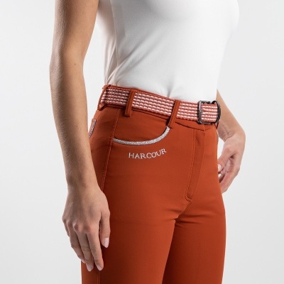 Pessoa com calças de montaria laranja HARCOUR e cinto xadrez com camisa polo branca