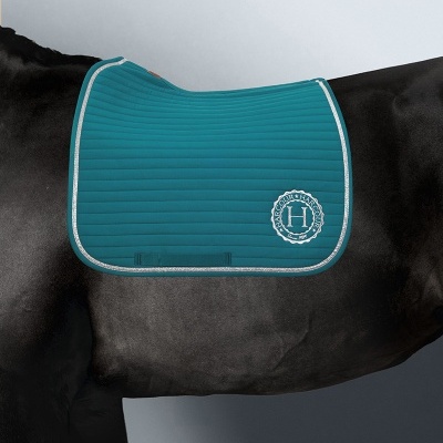 Manta de sela azul turquesa acolchoada com bordas cinzentas e logótipo branco com a letra H em cavalo preto