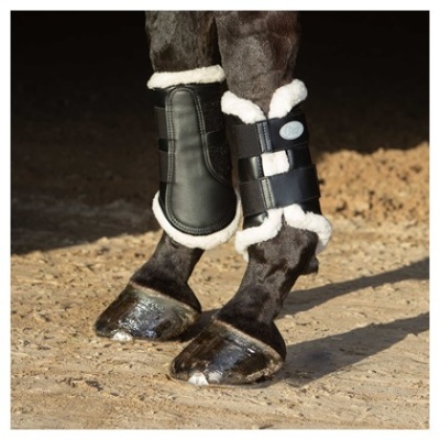 Pernas dianteiras de cavalo com proteções acolchoadas pretas e forro branco em chão de terra