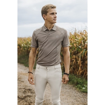 Homem com camisa polo cinza claro e calças brancas em caminho de terra junto a campo de milho