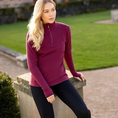 Mulher com camisola térmica rosa escuro e calças pretas sentada num muro de pedra num jardim