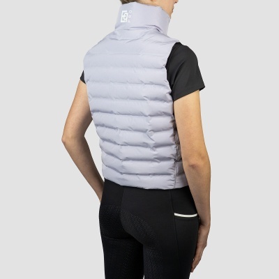 Colete acolchoado cinza claro de costas com gola alta e texto branco, mulher com t-shirt preta e calças pretas.