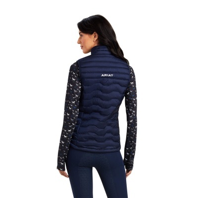 Mulher de costas a usar colete azul escuro acolchoado com logo branco e camisola preta com padrão de cavalos