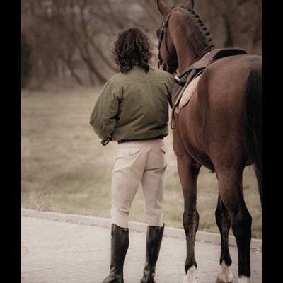 Homem com casaco verde e um cavalo castanho ao lado num espaço exterior