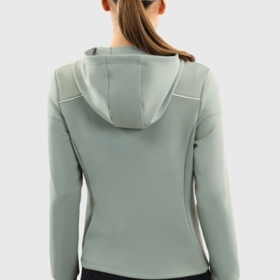 Pessoa vista de costas com casaco verde-claro com capuz e boné da mesma cor, usando calças pretas