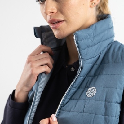 Colete feminino azul claro acolchoado com fecho de correr e símbolo redondo no peito, usado por mulher