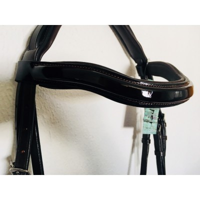 Freio em couro preto brilhante com fivelas prateadas pendurado numa parede