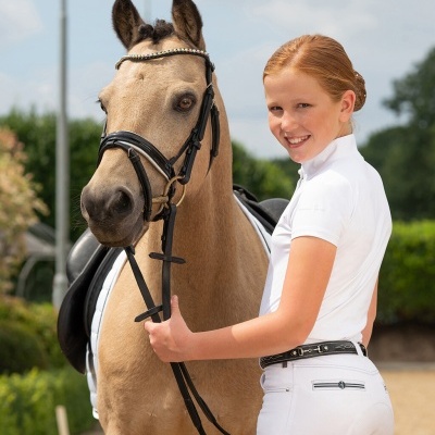 Menina com roupa branca de equitação e cavalo bege com arreios pretos ao ar livre