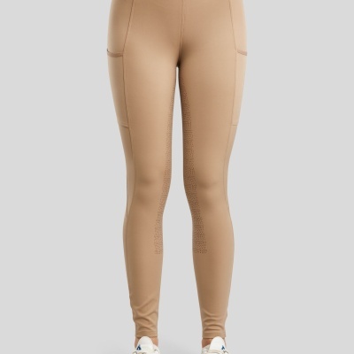 Leggings castanha clara com bolso e ténis brancos e pretos num fundo cinzento.