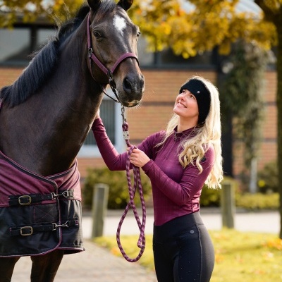Mulher com roupa desportiva segura cavalo com manta ao ar livre em ambiente de outono