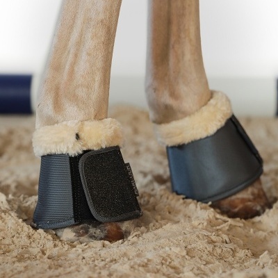 Proteção para pernas de cavalo em material preto com forro de pelúcia creme sobre areia
