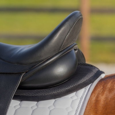 Sela de equitação preta sobre manta branca e cavalo castanho