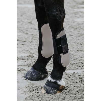 Perna de cavalo com proteção cinza claro e velcro preto num chão de areia