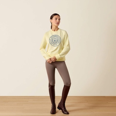 Mulher com camisola amarela, leggings castanhas claras e botas castanhas