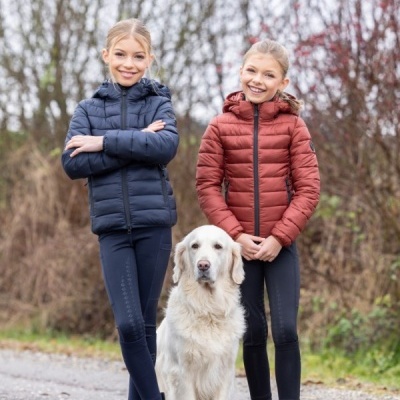 Duas meninas com casacos acolchoados e botas pretas posam ao ar livre com um Golden Retriever branco entre elas